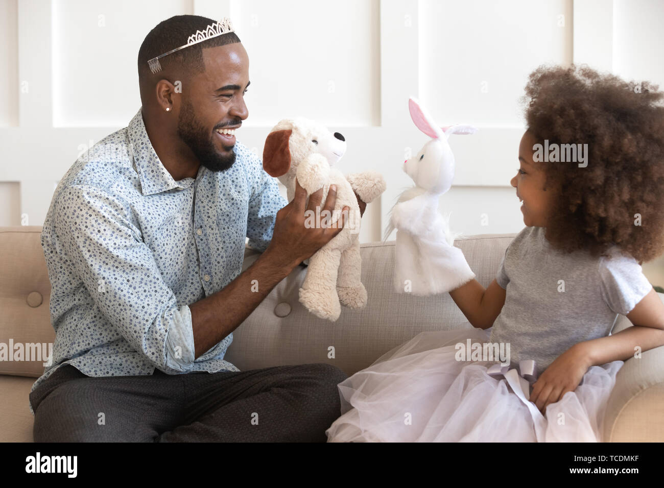 Happy african dad wearing crown holding toys playing with daughter Stock Photo