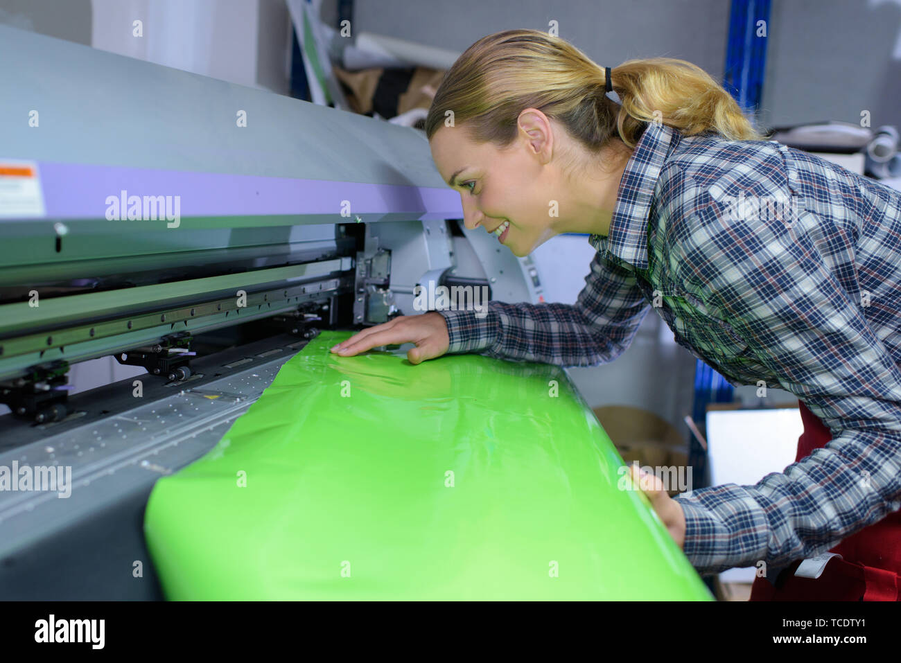 female worker inserting shiny green paper in machine Stock Photo