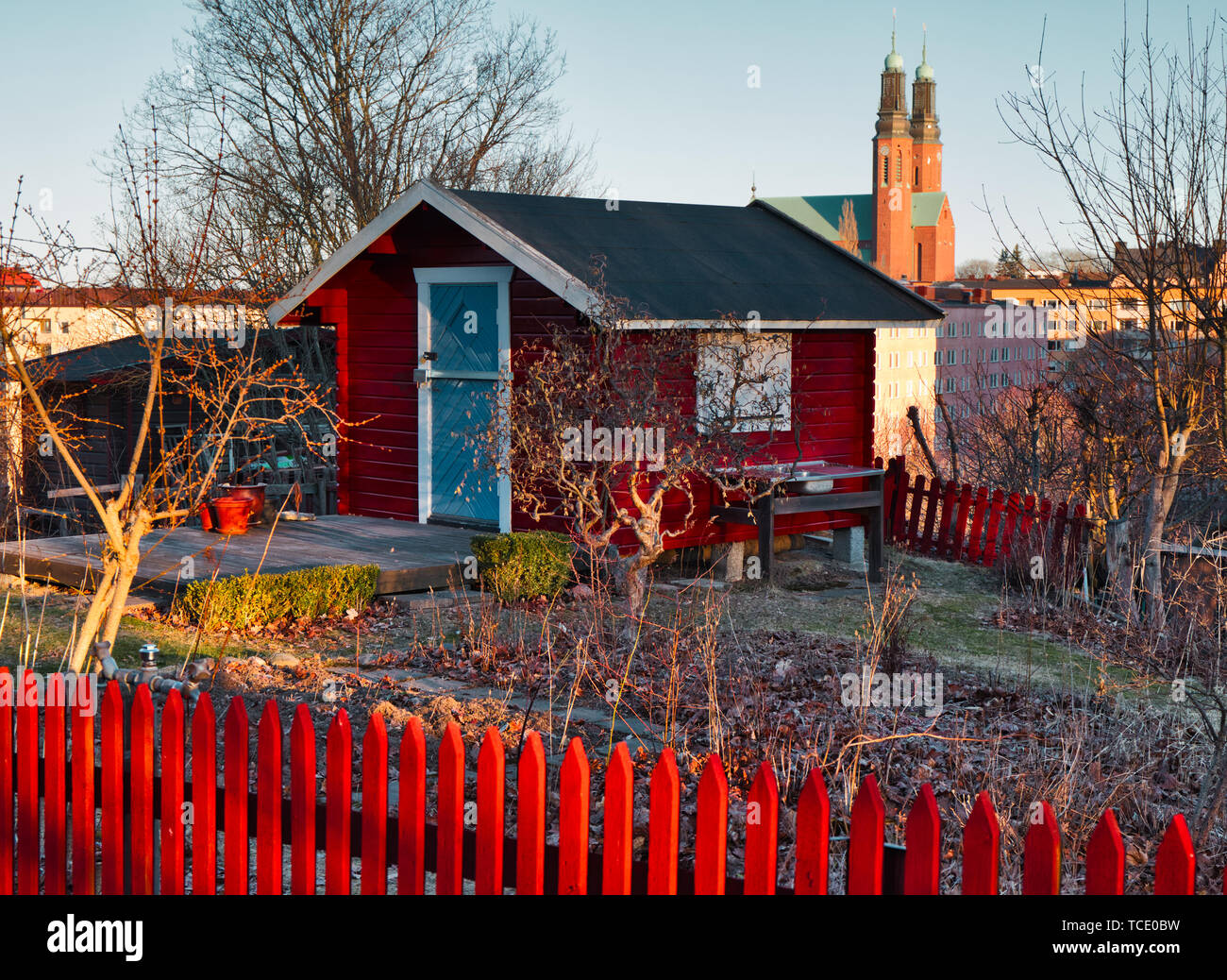 Falun red allotment cottage and fence with the towers of Hogalid Church