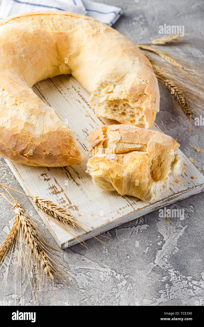 Wheat round bread in the form of a ring and spikelets on a wooden cutting board on a light concrete background. Big bagel Stock Photo