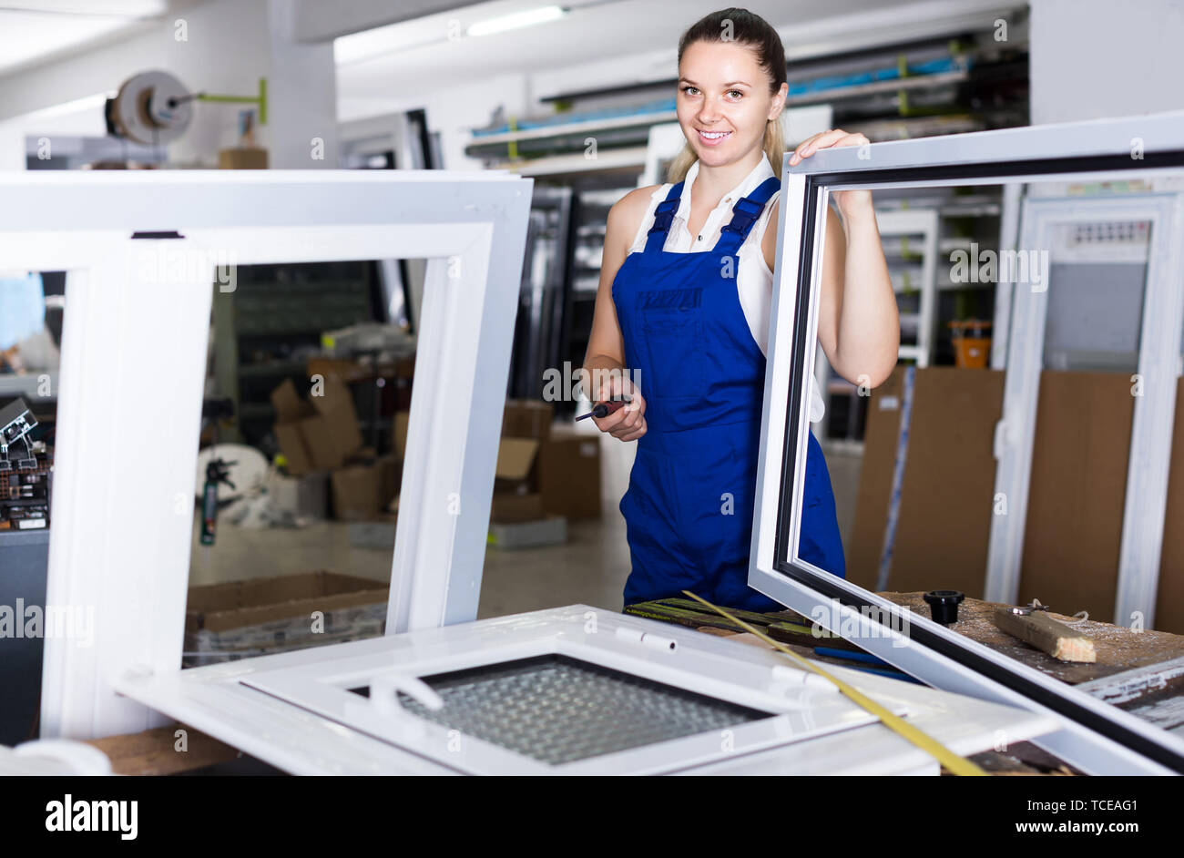 Young american female worker assembling metal-plastic window in workshop, using screwdriver Stock Photo