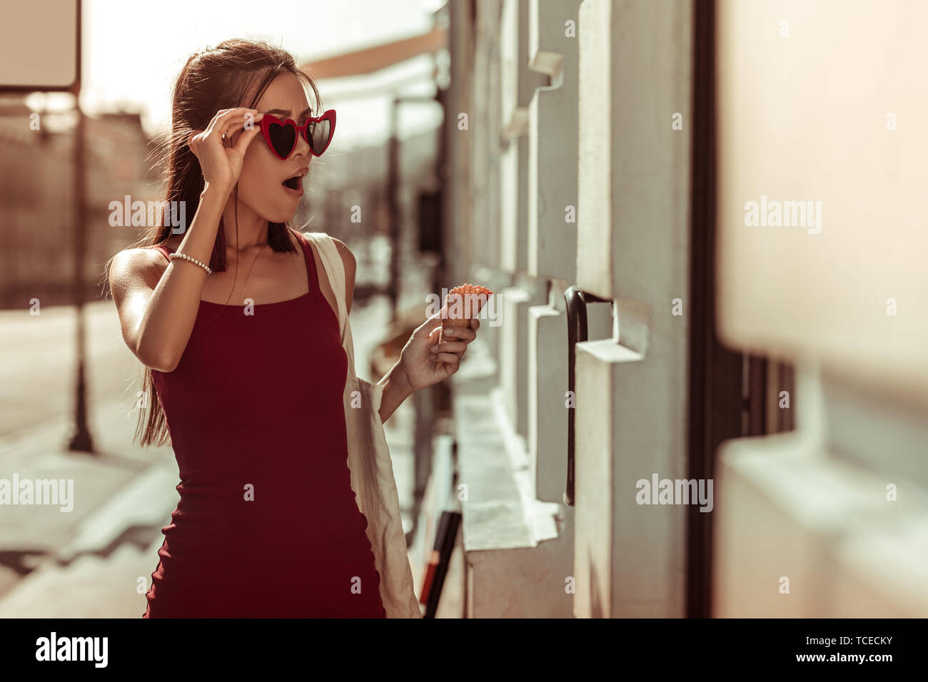 Shocked woman. Dark-haired slim hot nice-appealing bewitching woman in trendy eyeglasses and red dress feeling shocked while walking the streets Stock Photo