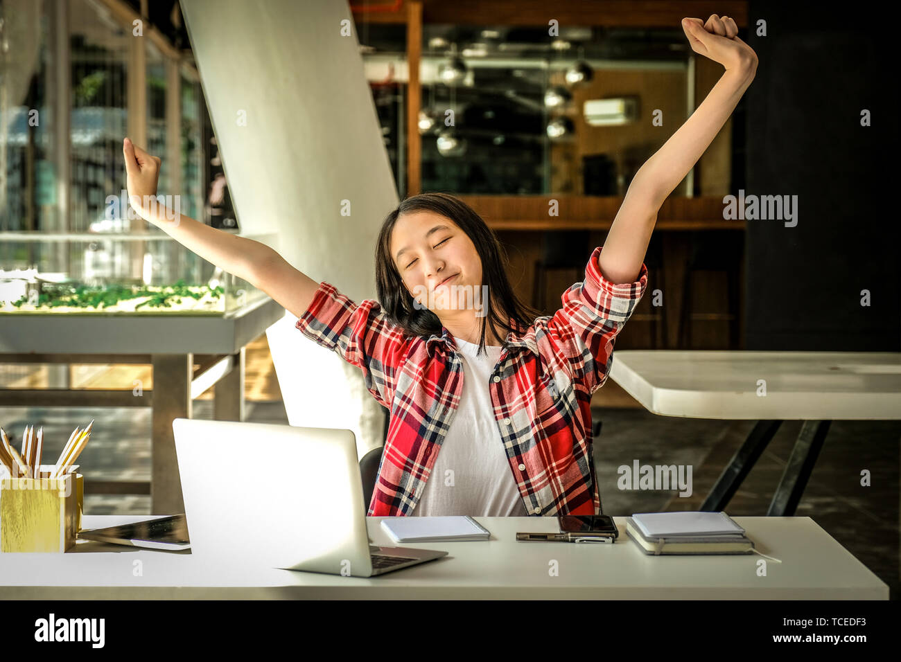 relaxed asian woman girl teenager stretching arms above head relaxing resting at co-working space Stock Photo