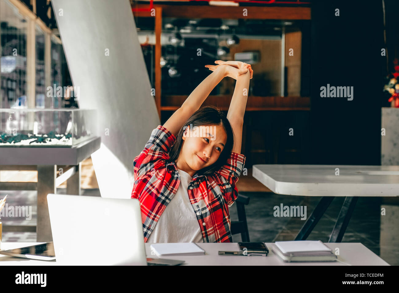 relaxed asian woman girl teenager stretching arms above head relaxing resting at co-working space Stock Photo