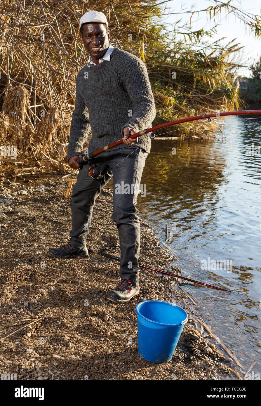 Portrait of afro fisherman standing near river and pulling fish Stock Photo