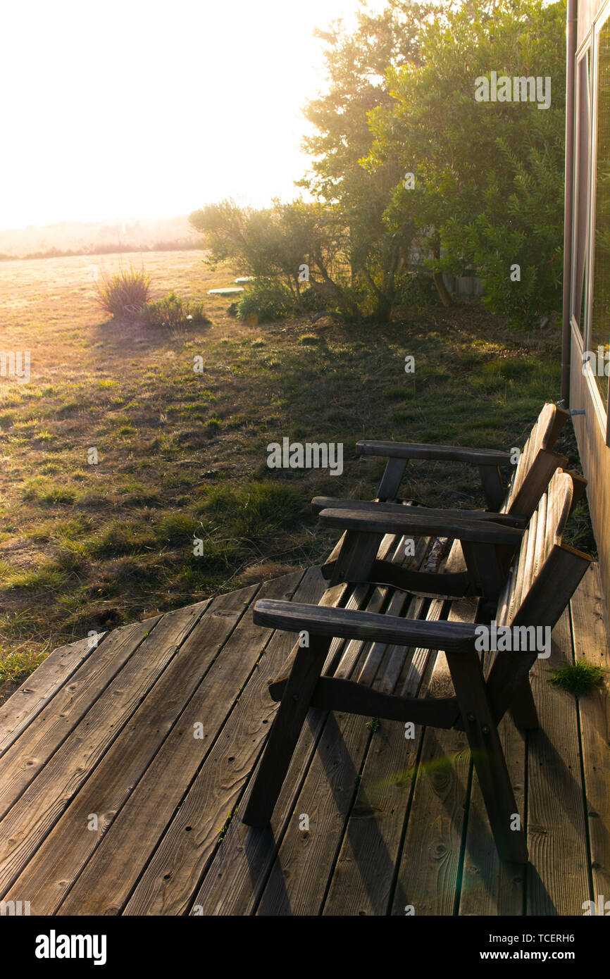 Two rustic wood chairs on a wood deck with a sunset lens flare and ...