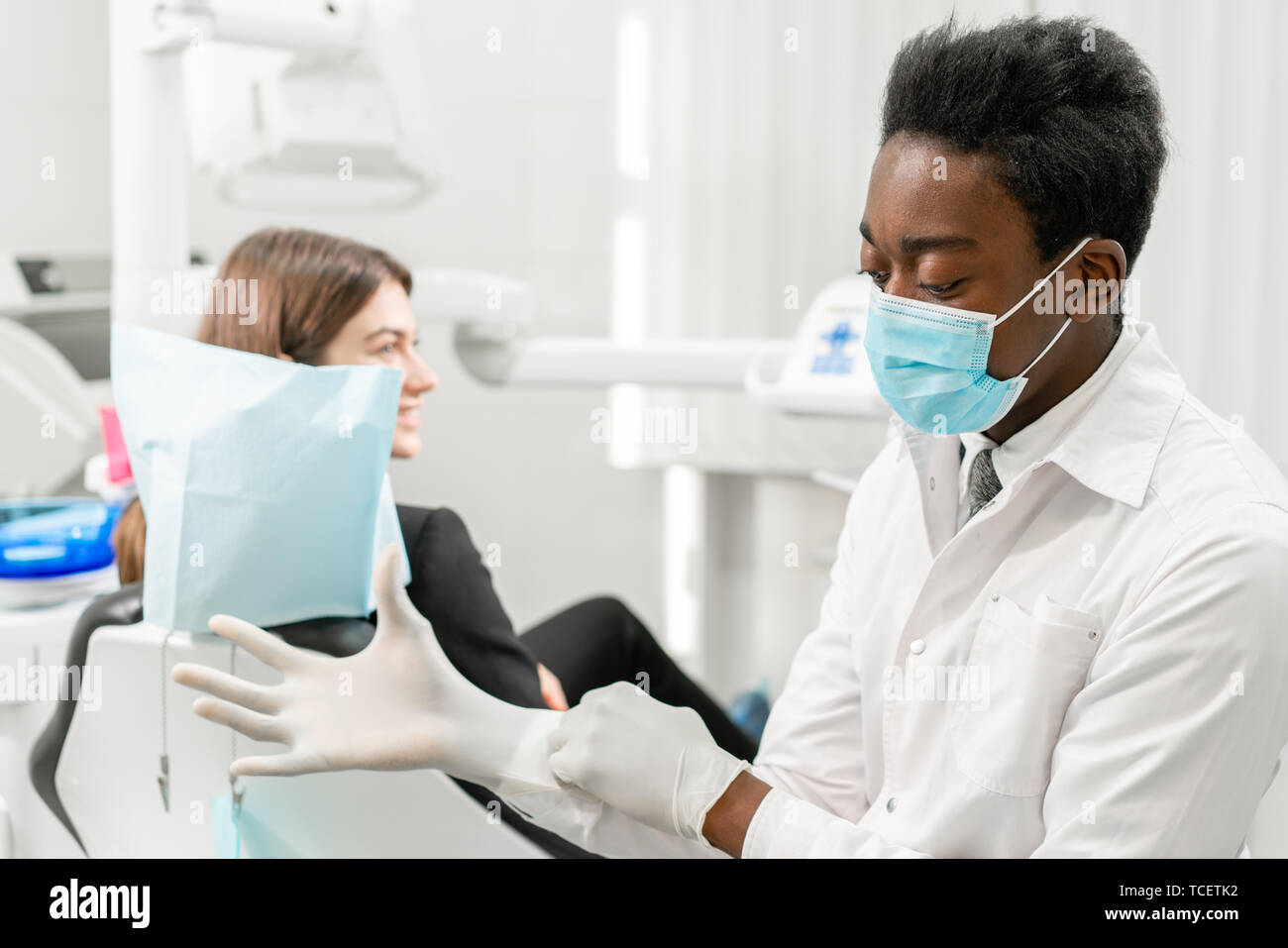 The doctor puts on rubber gloves. Young African male dentist with a
