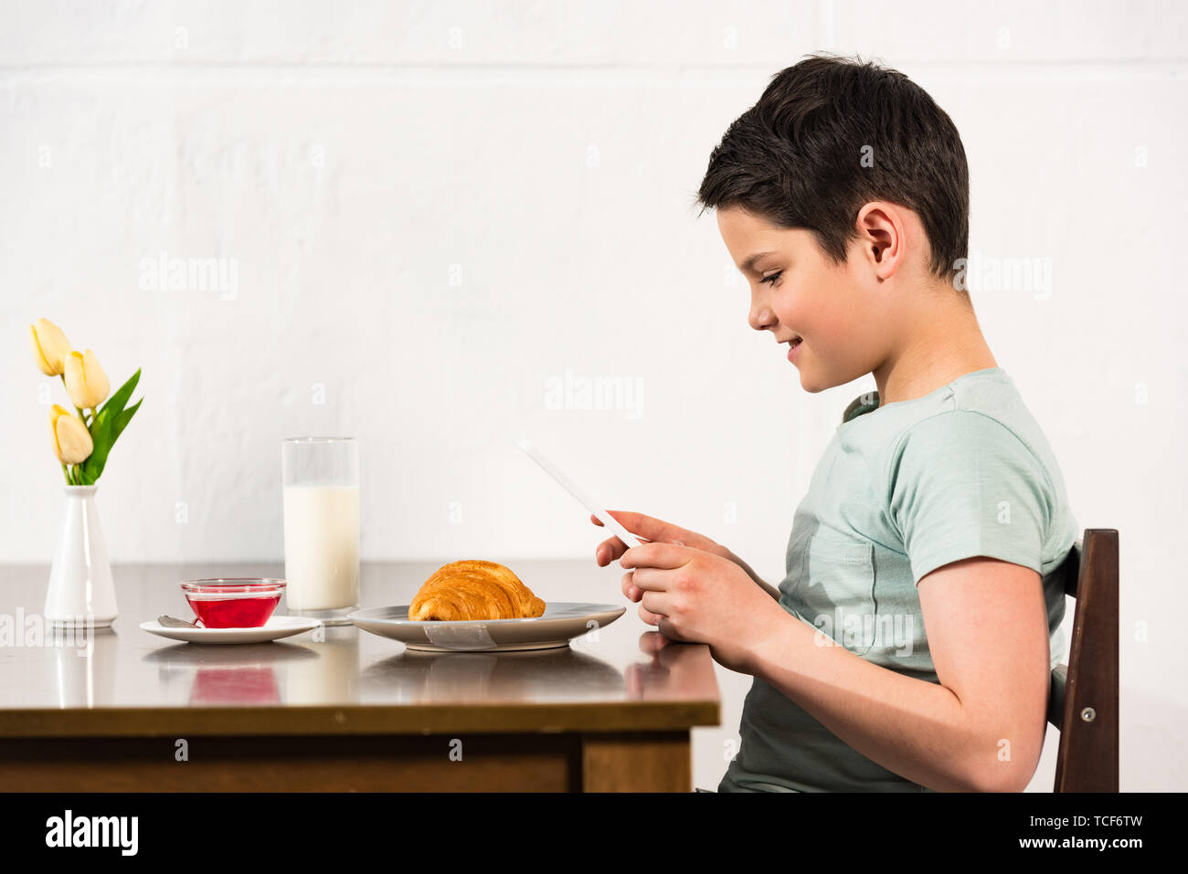 side view of smiling boy using digital tablet during breakfast in kitchen Stock Photo