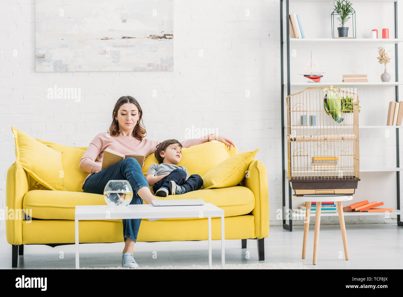 attractive woman with adorable son resting on yellow sofa in spacious living room Stock Photo