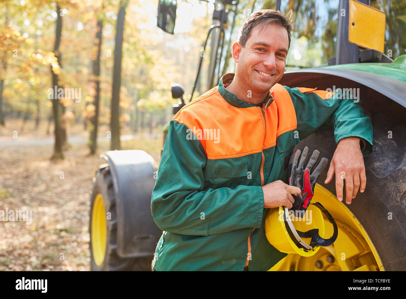Satisfied forest worker as a driver is leaning against the forwarder after the timber harvest Stock Photo