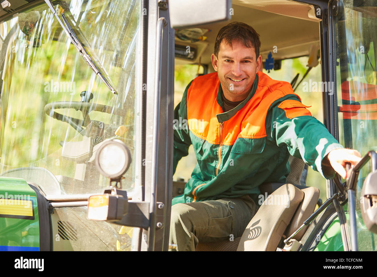 Smiling forest worker is sitting in the cabin of a forest tractor in the forest Stock Photo