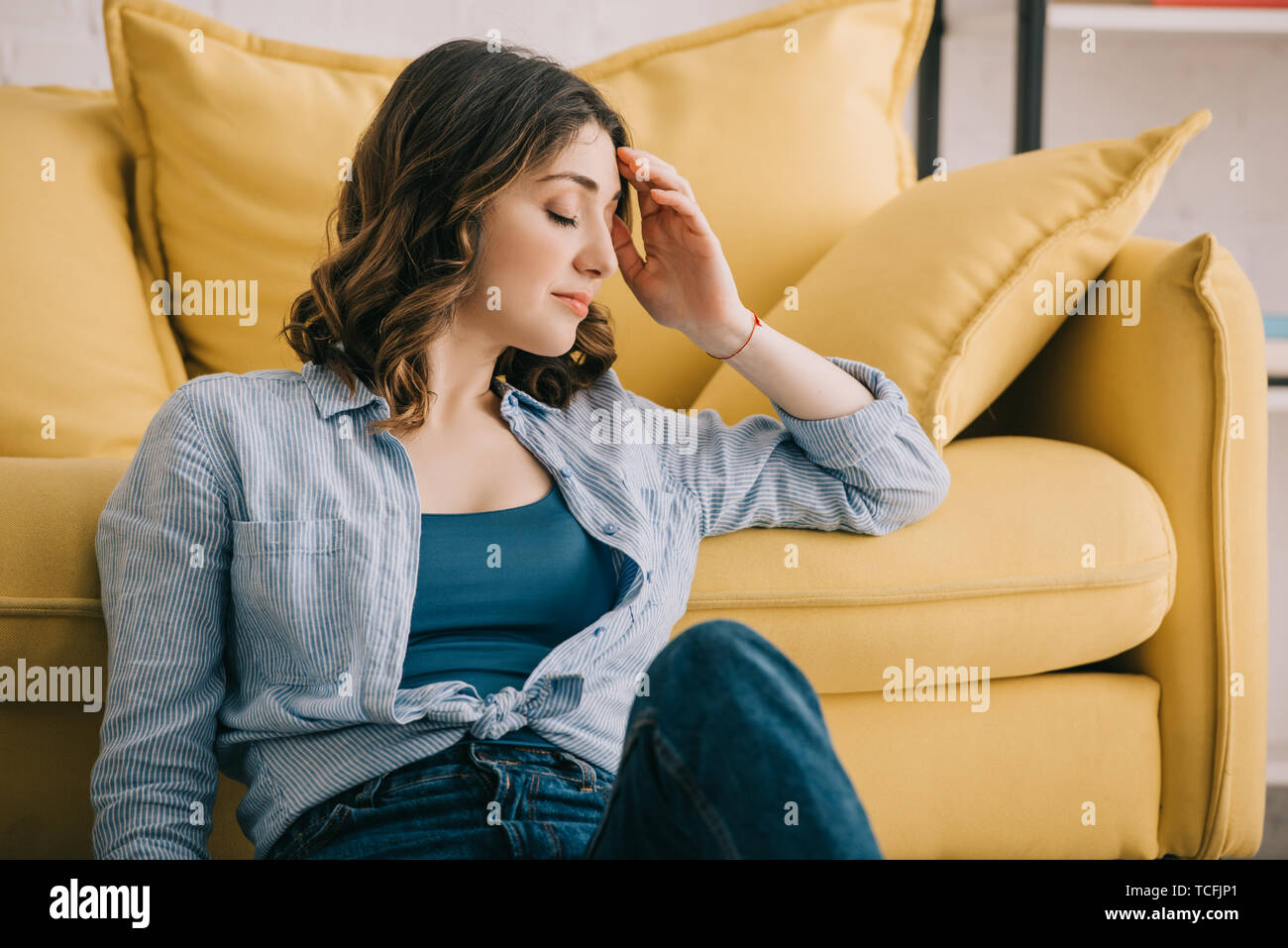 Tired woman sitting near yellow sofa with closed eyes Stock Photo - Alamy