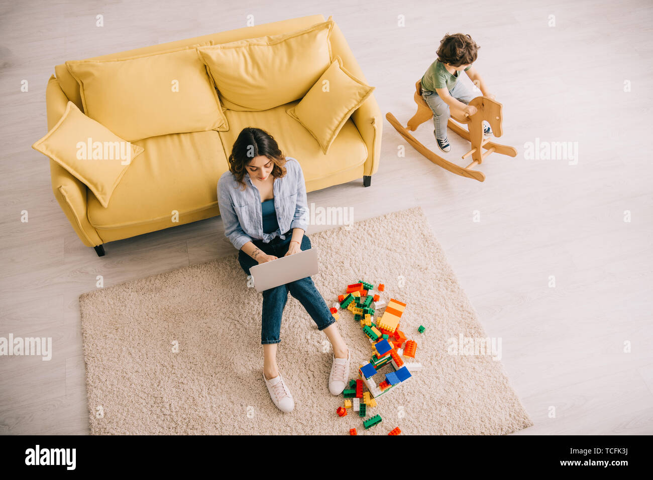 Overhead View Of Mother Using Laptop While Son Sitting On Rocking