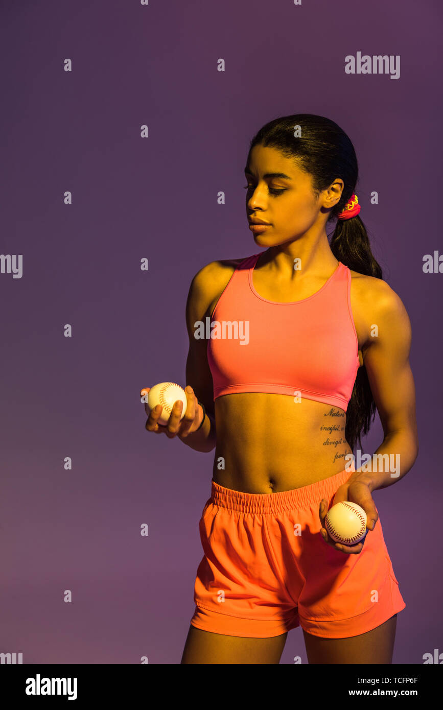 attractive sportive african american girl in pink sports bra and shorts holding balls on purple background Stock Photo