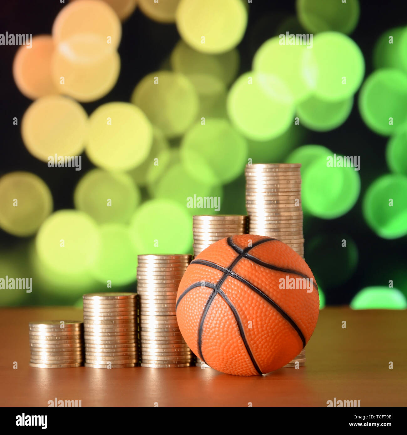 Basketball and stacks of golden coins in growth graph on the blurred bokeh background. Sport betting concept Stock Photo