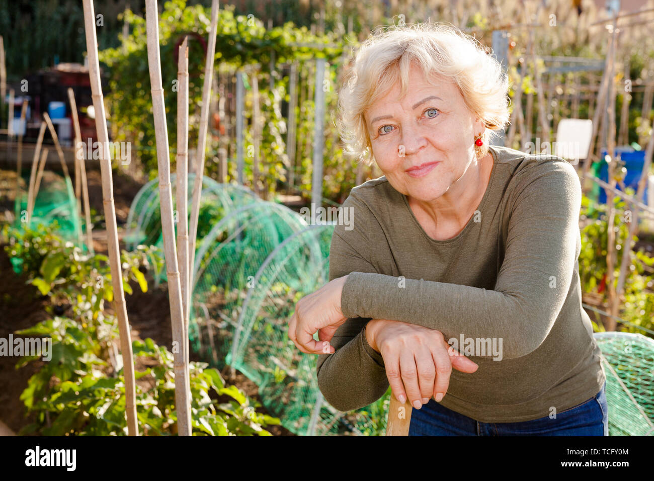 Portrait Of Positive Mature Woman Among Plants In Backyard Garden Stock 