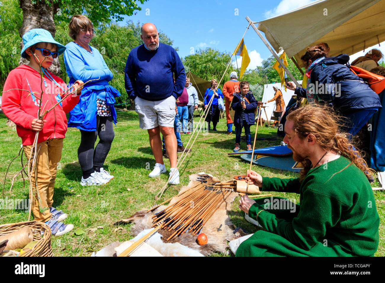 Le Medieval Weekend re-enactment event at Sandwich, England. Members of the public standing looking at a long bow and collection of arrows while taking to a medieval arrow maker on the grass in park. Stock Photo