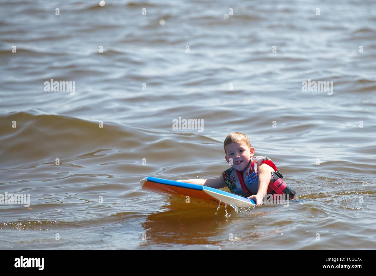 A young boy paddles on a surfboard in the calm water Stock Photo