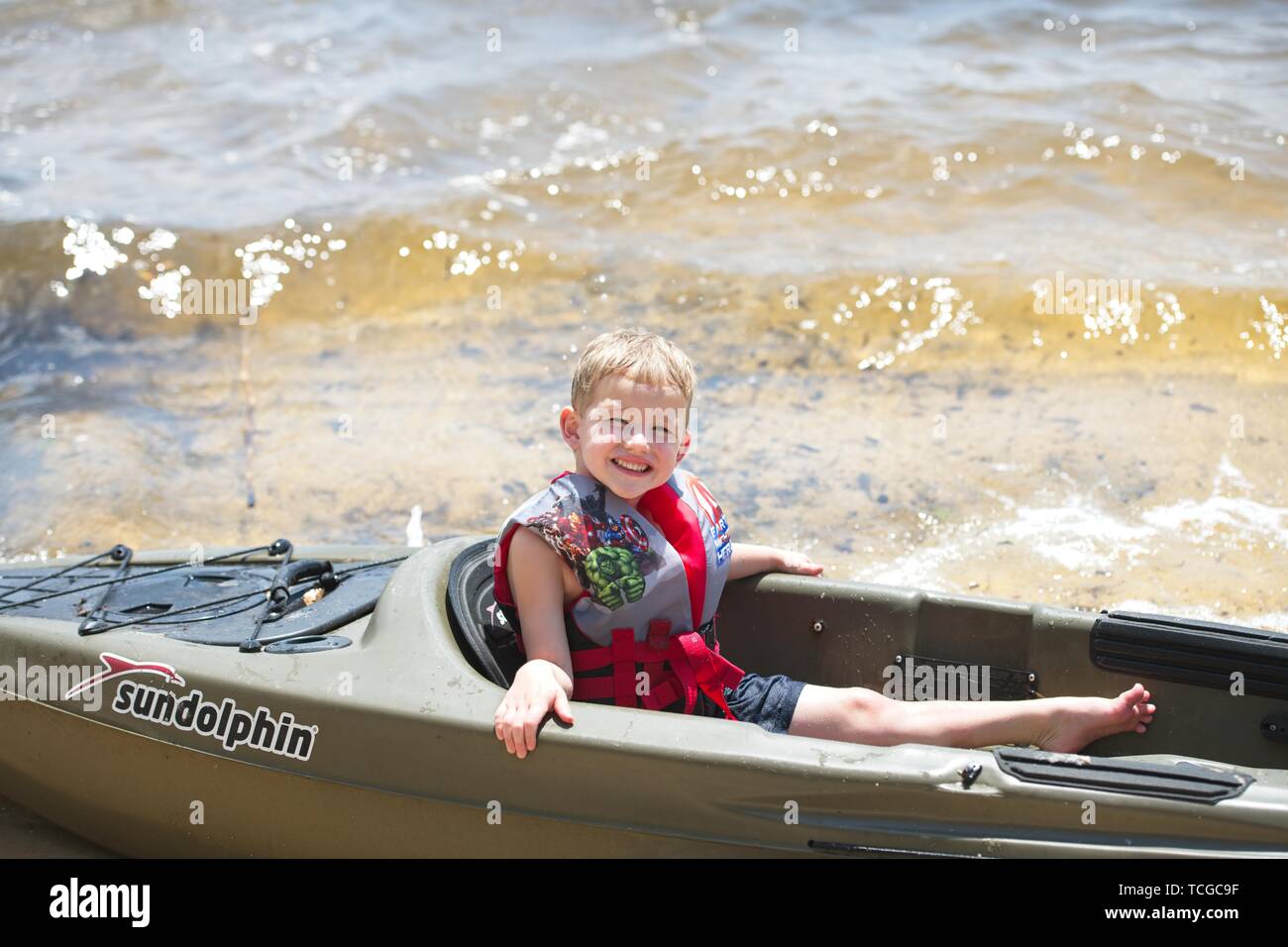 A young boy sits in a kayak at the shoreline of the bay Stock Photo