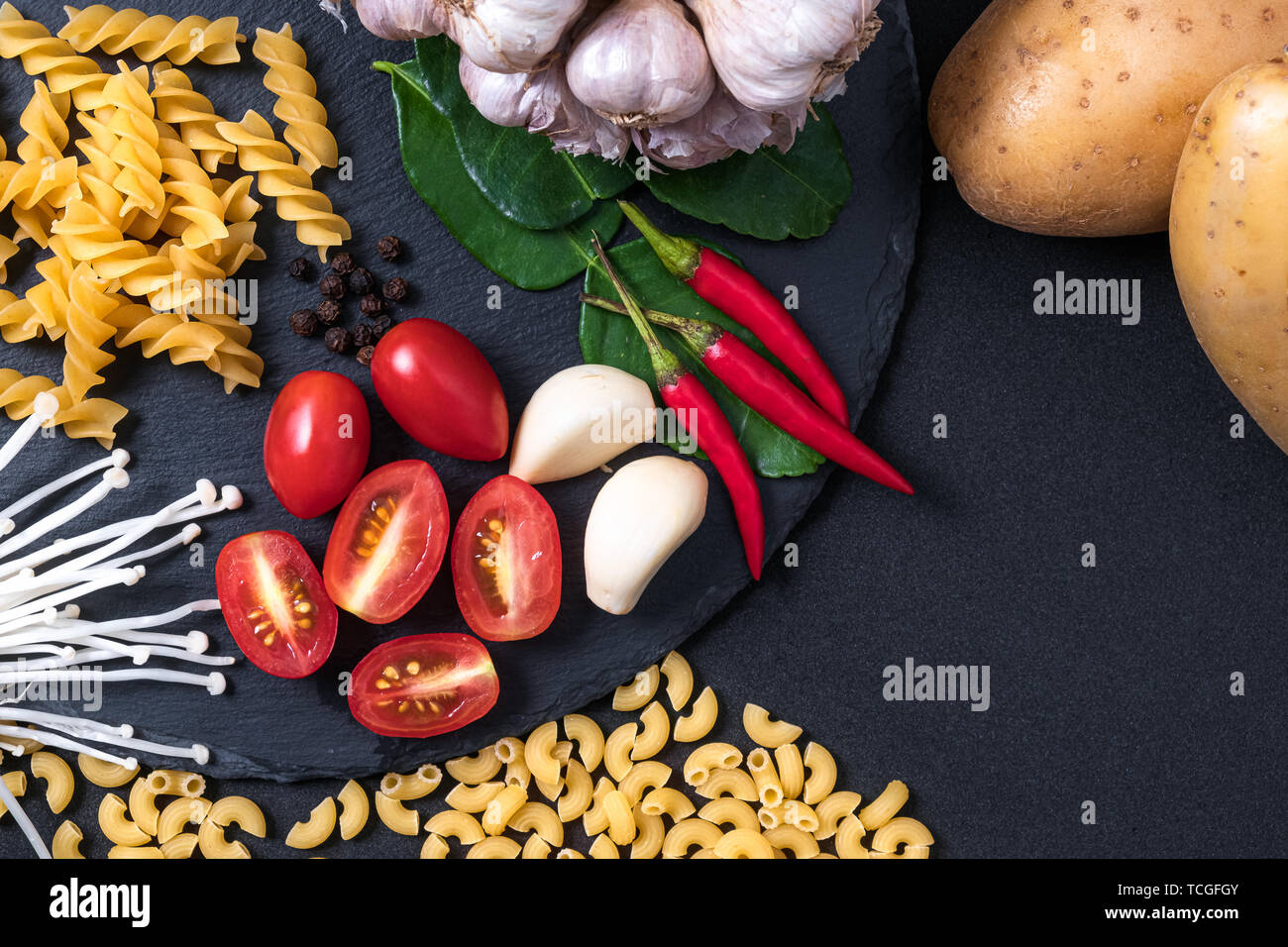 top view of fresh ingredients. Healthy cooking background with organic vegetables and pastas for vegan on black slate . tomato , garlic and fresh chil Stock Photo