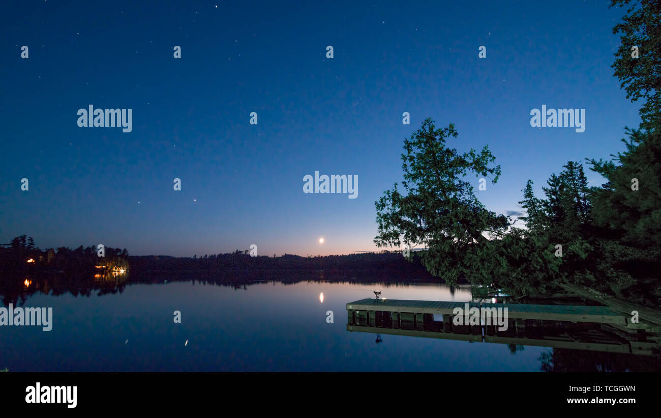 Tranquil peaceful late sunset - early evening on Hungry Jack Lake with dock / pier, moon, stars, and cabins off the Gunflint Trail in Northern Minneso Stock Photo