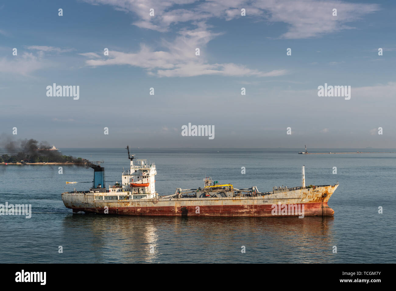 Makassar, Sulawesi, Indonesia - February 28, 2019: Rusty cement carrier Cemcon ship sails into port exhausting black smoke. Blue sea and sky. Stock Photo