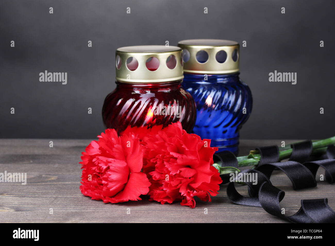 Memory lantern with candles, red carnations and ribbon on wooden table on grey background Stock Photo