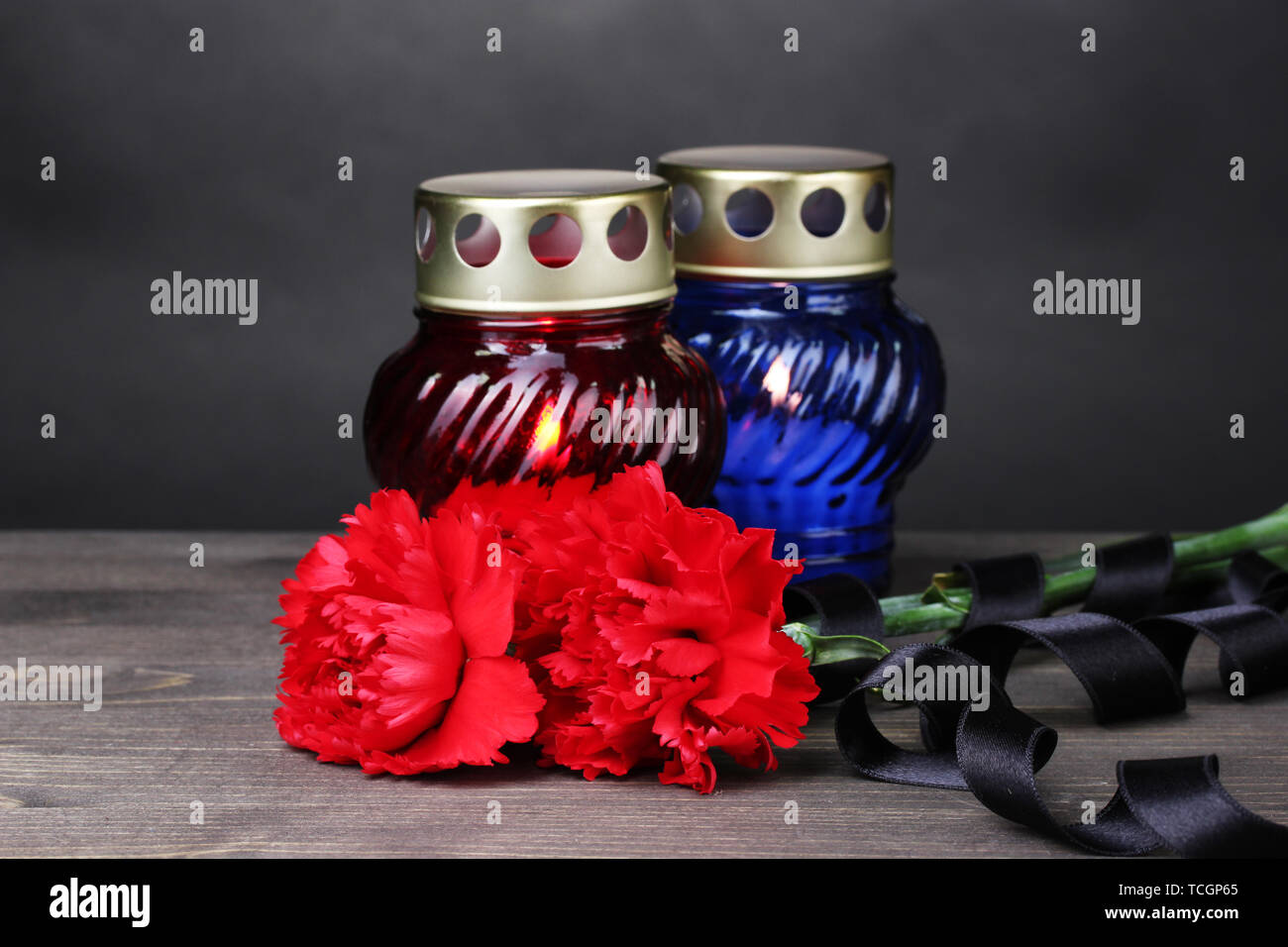 Memory lantern with candles, red carnations and ribbon on wooden table on grey background Stock Photo
