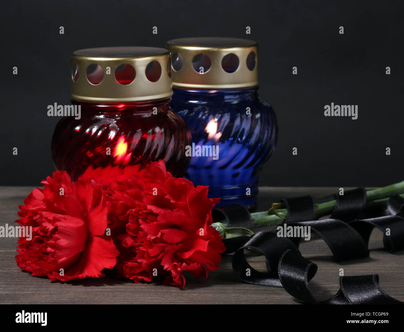 Memory lantern with candles, red carnations and ribbon on wooden table on grey background Stock Photo