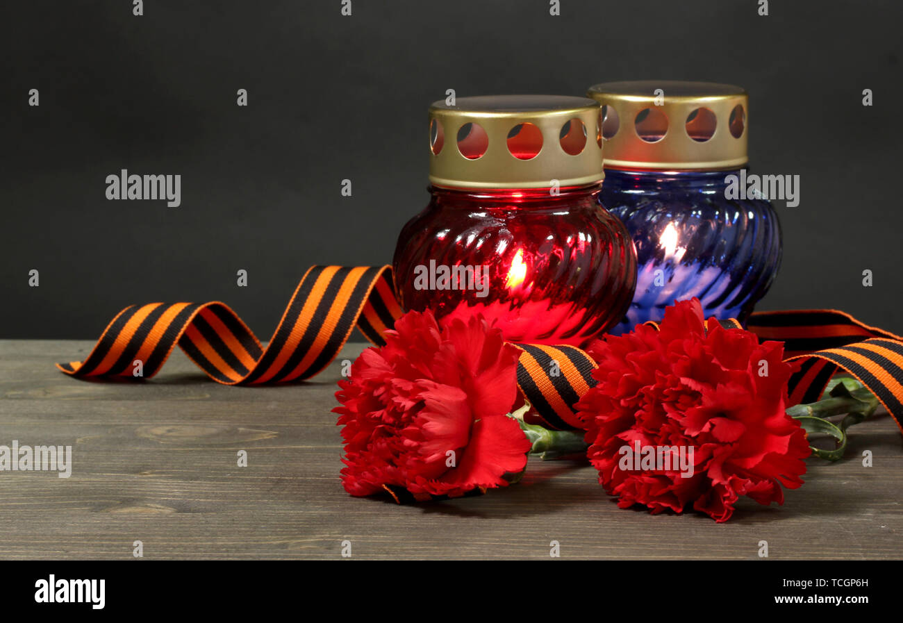 Memory lantern with candles, red carnations and St. George ribbon on wooden table on grey background Stock Photo