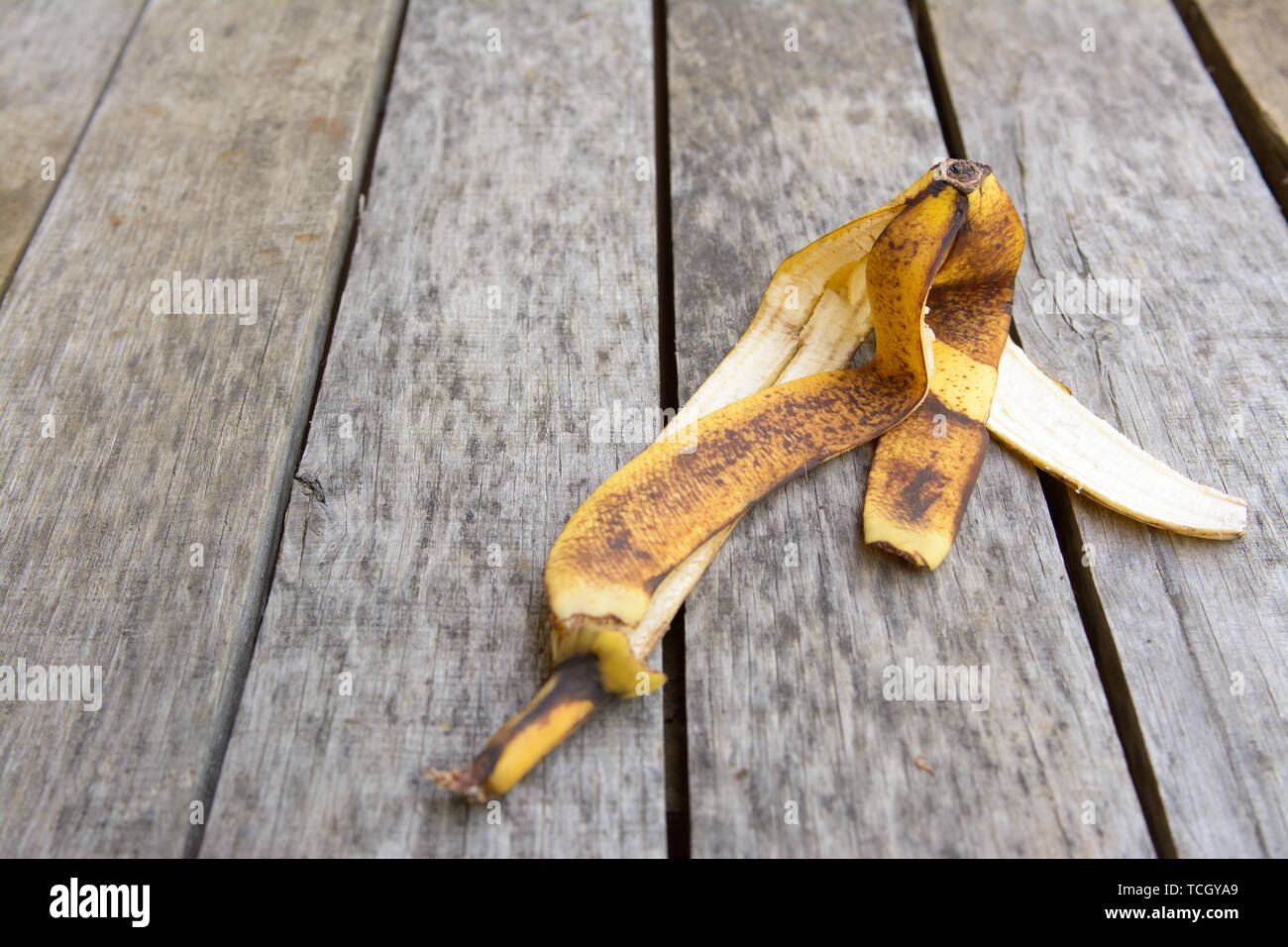 Brown and yellow crumpled banana peel lying on old grey with dark spots wooden surface Stock
