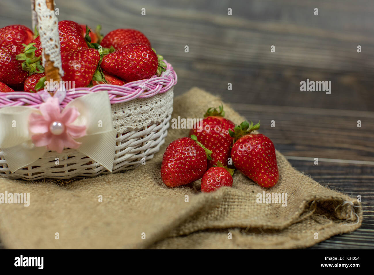 Strawberries in a small basket on the wooden table - close up. Place ...
