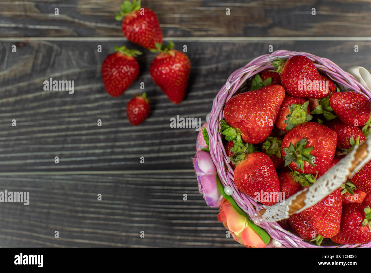 Strawberries in a small basket on the wooden table - close up. Place ...