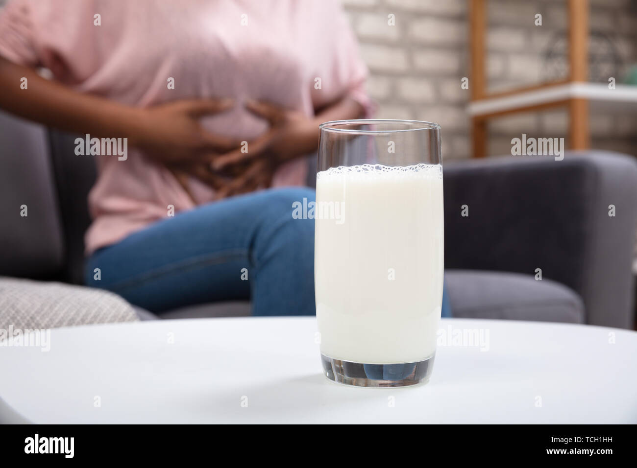 Woman Suffering From Stomach Pain With Glass Of Milk On White Desk