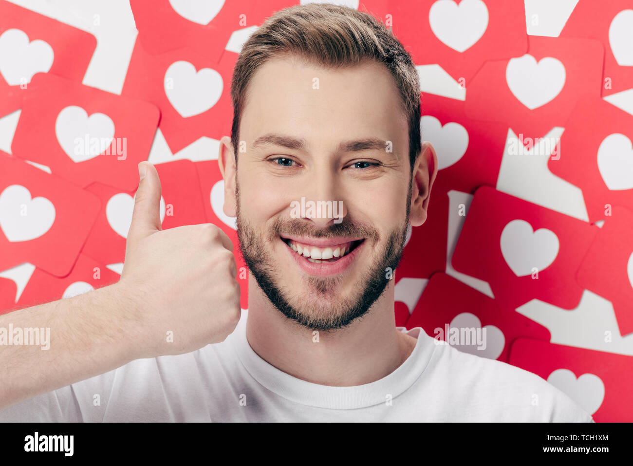 handsome cheerful man showing thumb up near red paper cut cards with