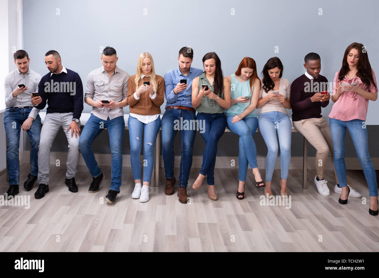 Multi-ethnic Young People Leaning Near Table In Row Using Smartphone Stock Photo