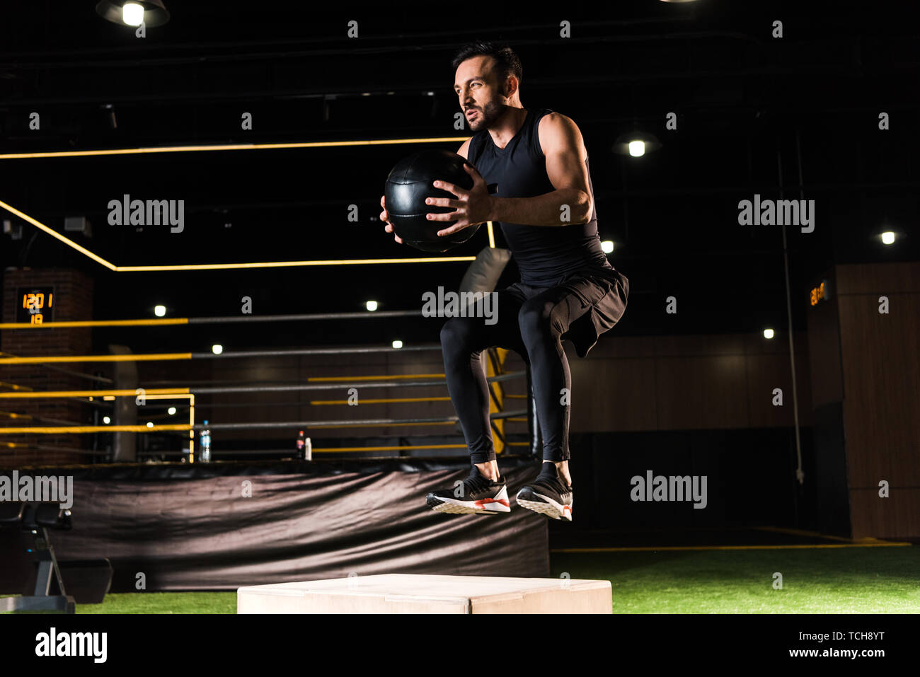 low angle view of serious man jumping on squat box while holding ball Stock Photo