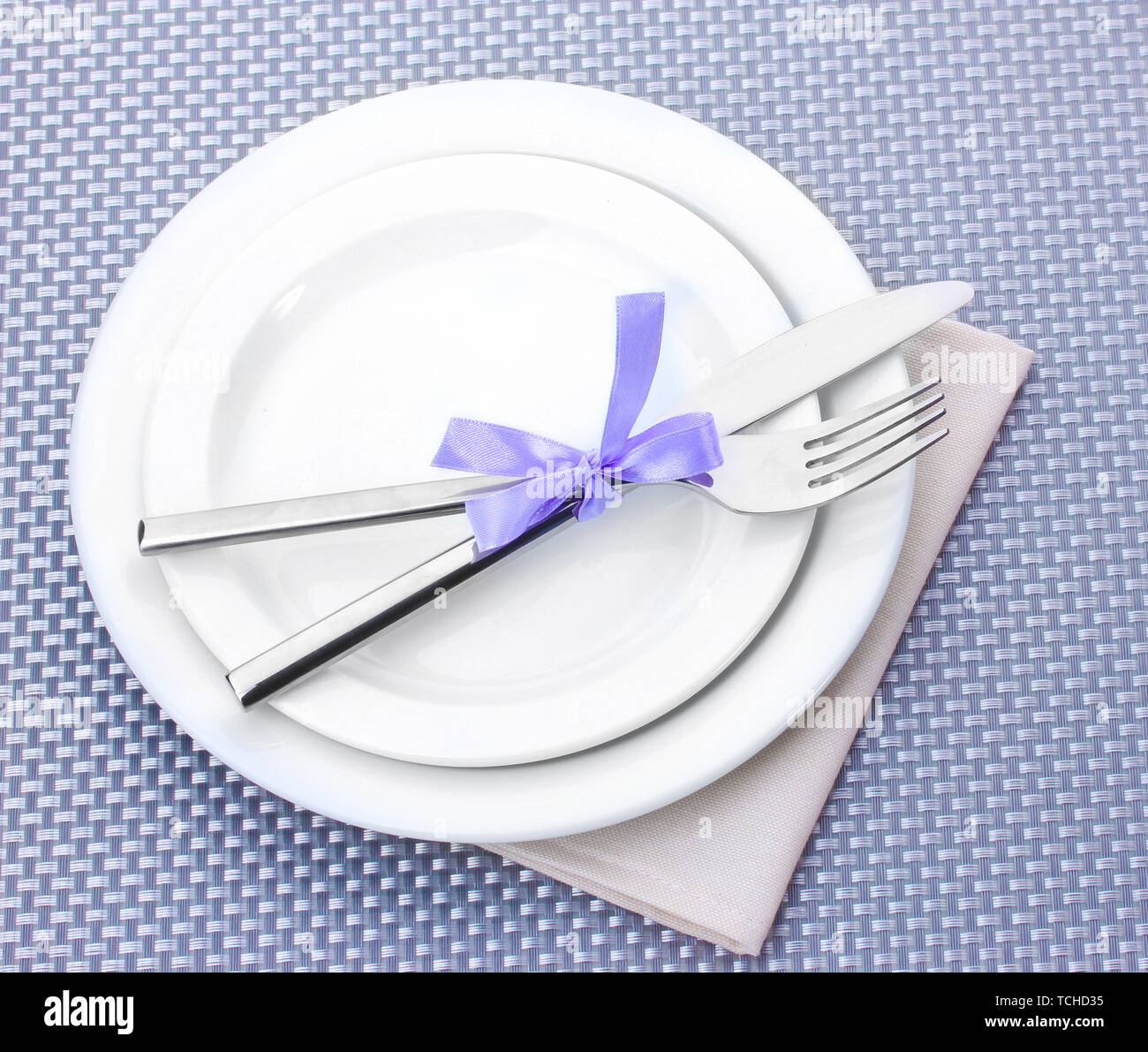 White empty plates with fork and knife tied with a ribbon on a grey ...