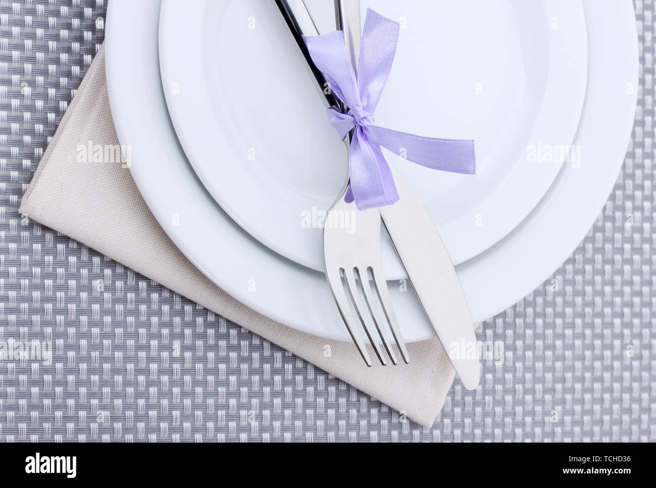 White empty plates with fork and knife tied with a ribbon on a grey ...