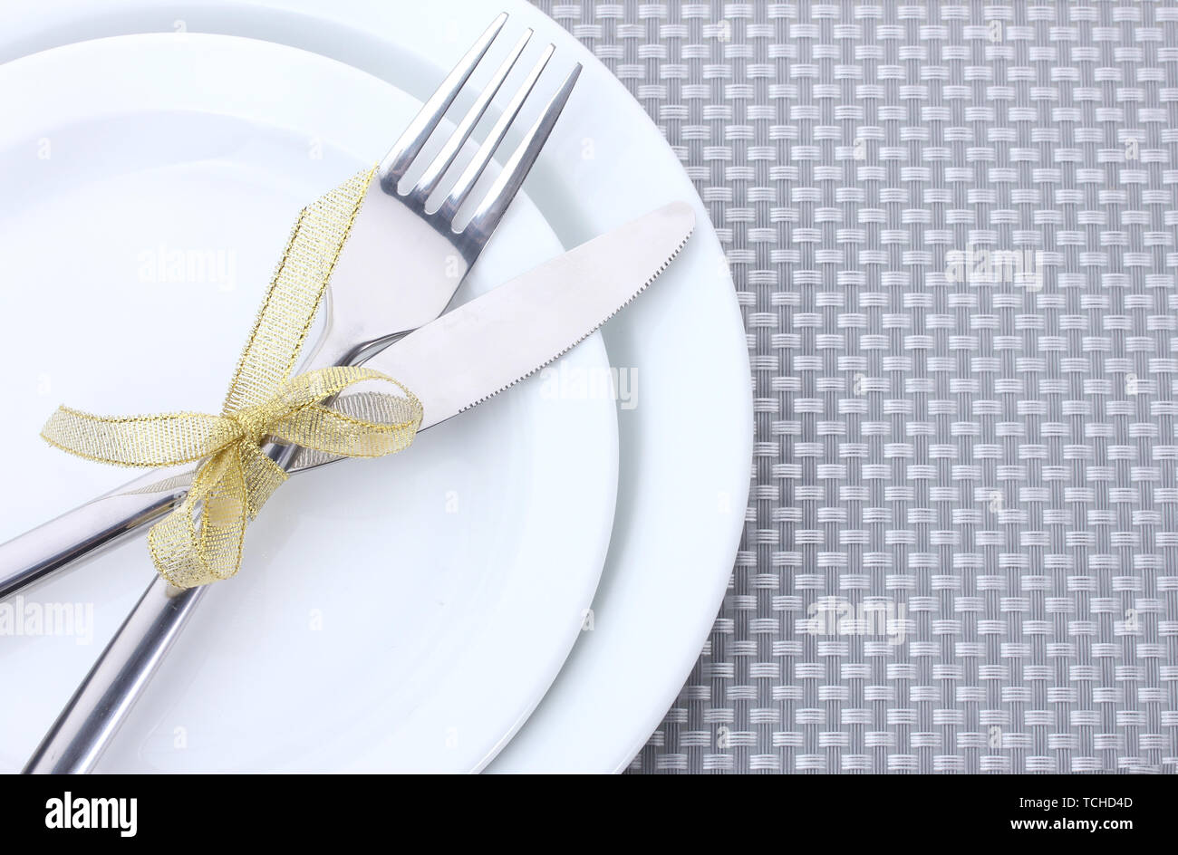 White empty plates with fork and knife tied with a ribbon on a grey ...