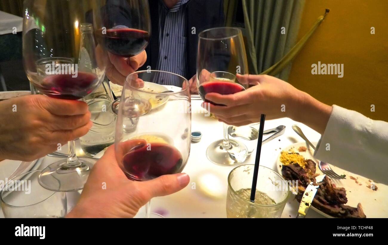four hands holding red wine and doing cheers to celebrate in a restaurant. Stock Photo