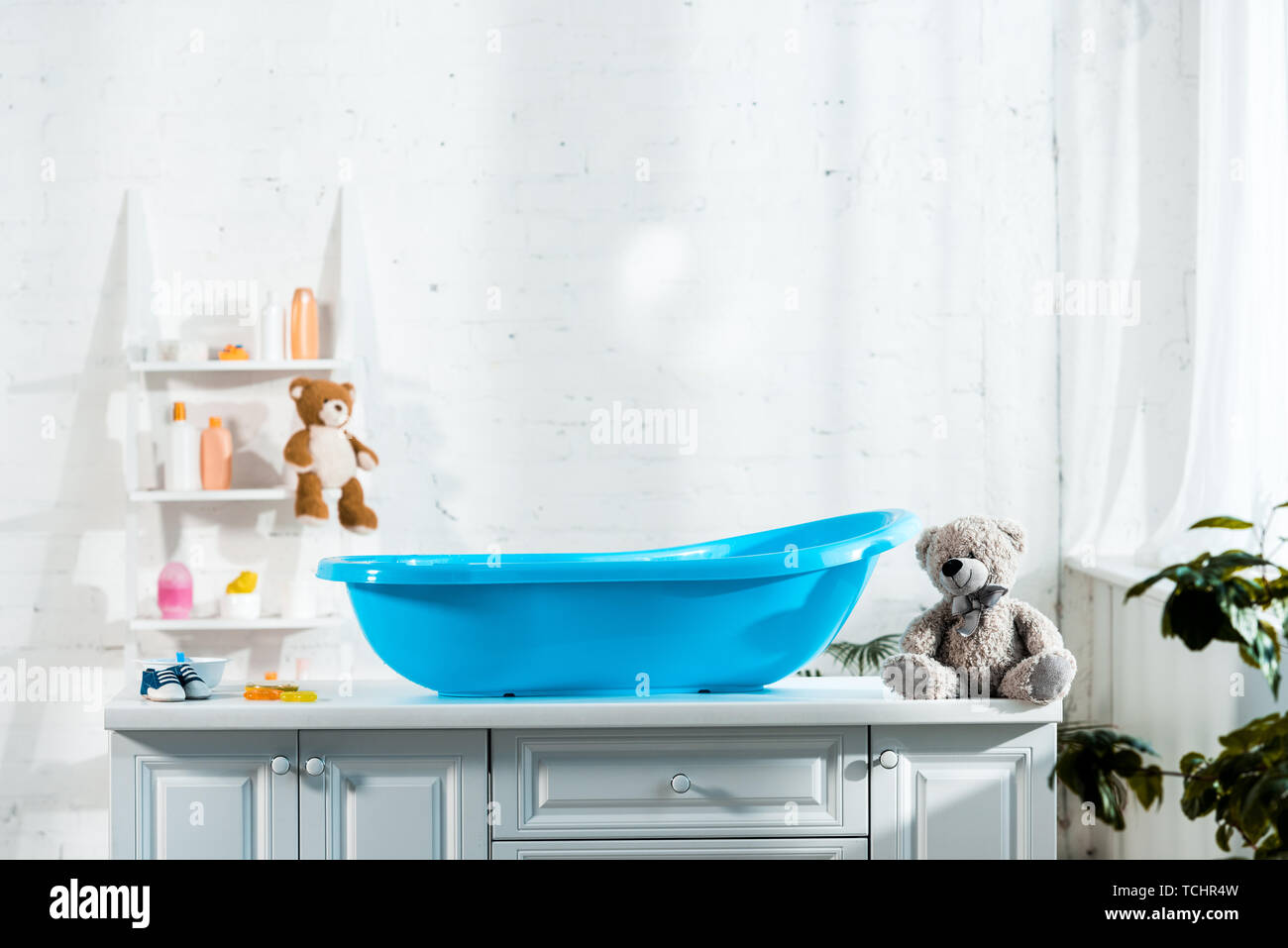 blue baby bathtub near teddy bear and baby sneakers in bathroom Stock