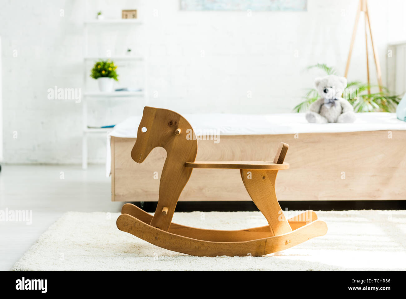 selective focus of wooden rocking horse near bed with white bedding and teddy bear Stock Photo