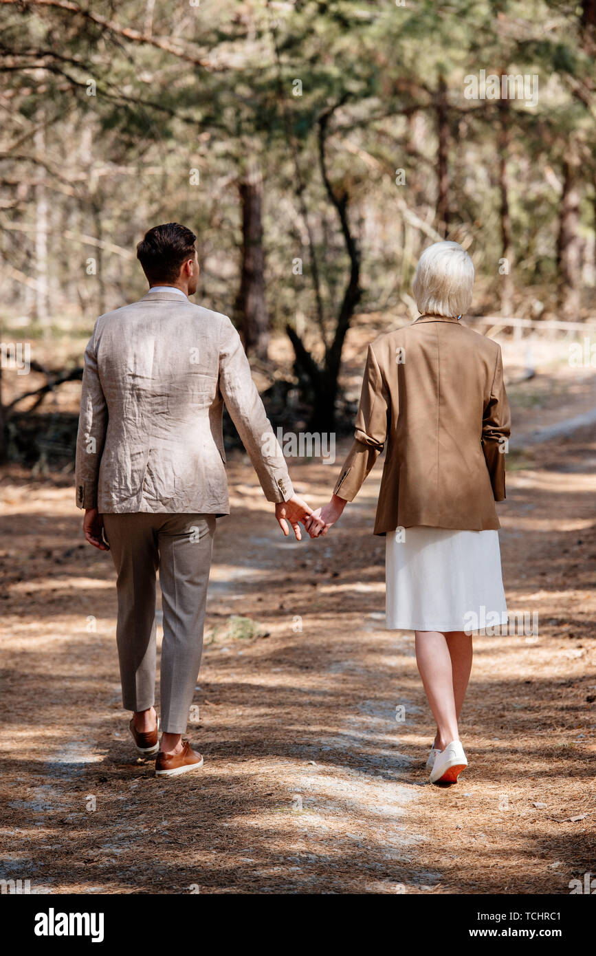 back view of stylish couple holding hands and walking in forest Stock ...