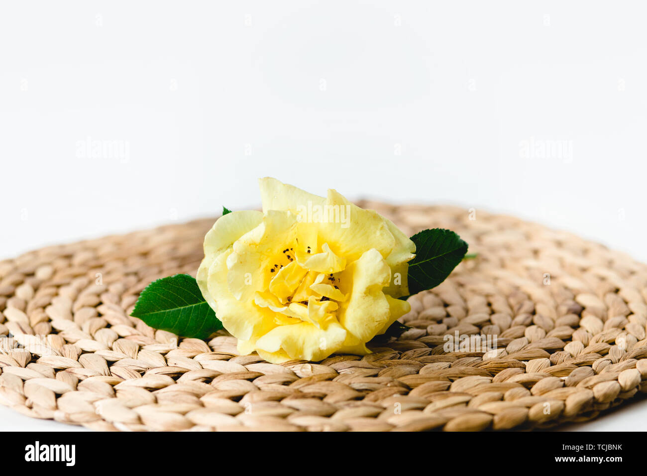 Yellow rose in glass vase on a nature wicker napkin on white background
