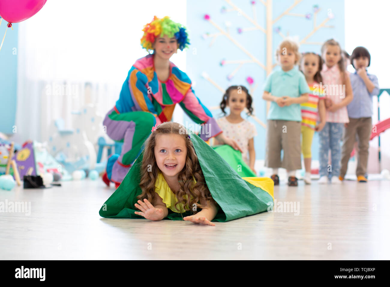 Kids playing with clown on birthday party in entertainment centre. Little girl climbing through tunnel Stock Photo