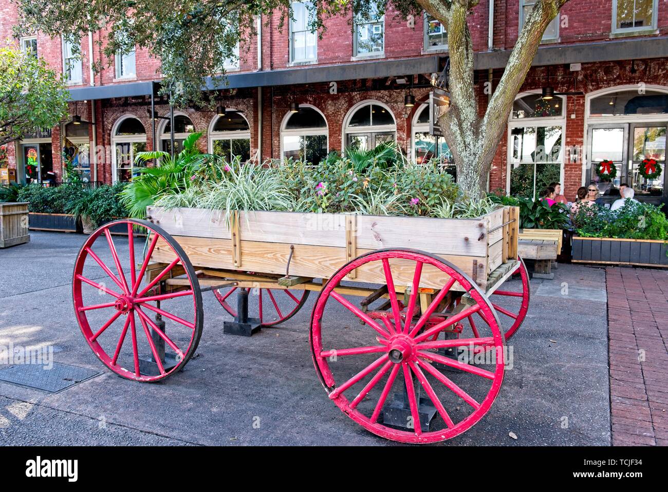 A wagon wheel cart filled with flowers sits in the walk among historic buildings in Savannah, Georgia Stock Photo