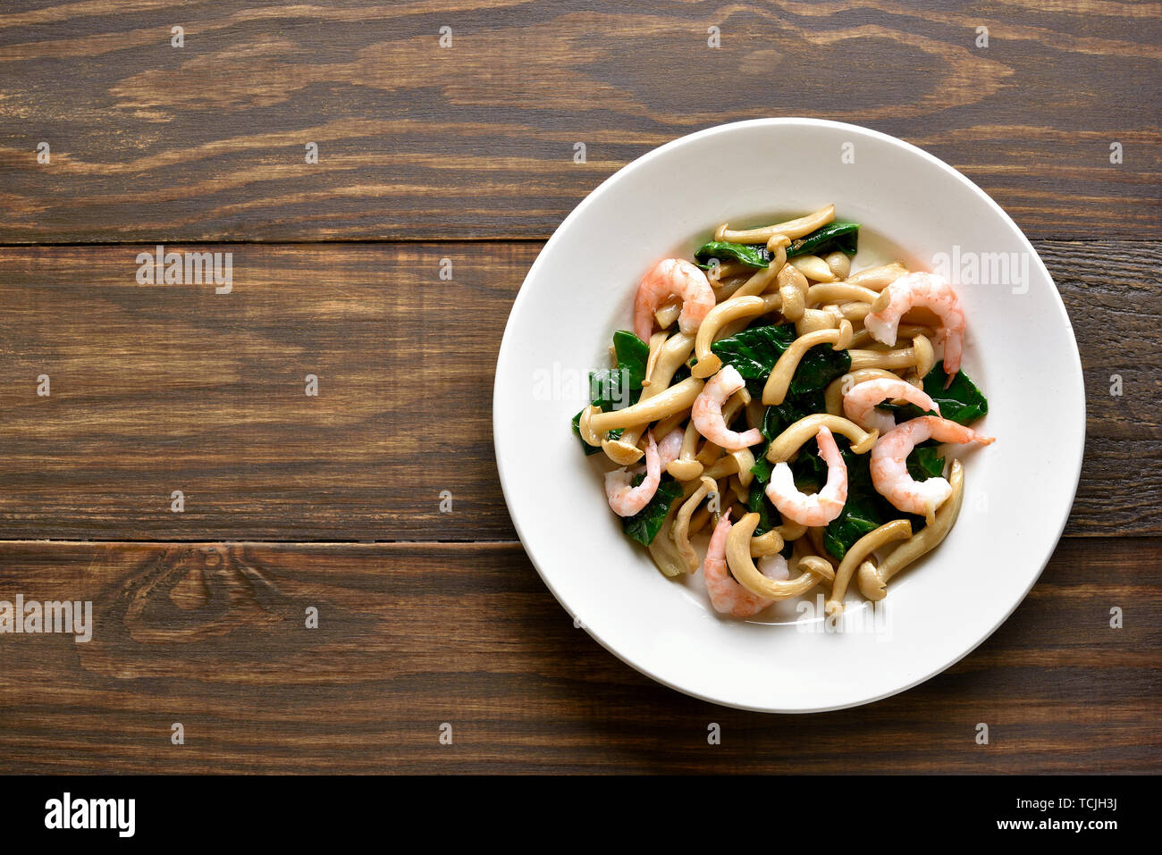 Stir-fried white beech mushrooms with leaves of spinach and shrimps on wooden background with copy space. Top view, flat lay Stock Photo