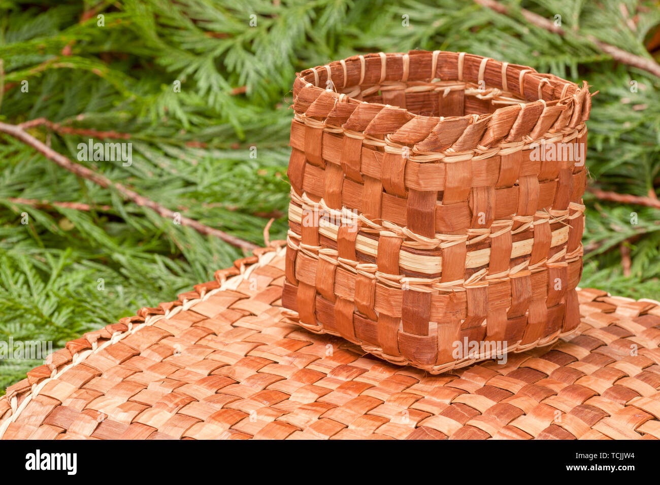 Hand-woven mat and basket made from the pliant inner bark of a Western Red Cedar tree, resting on Western Red Cedar branchlets. Stock Photo