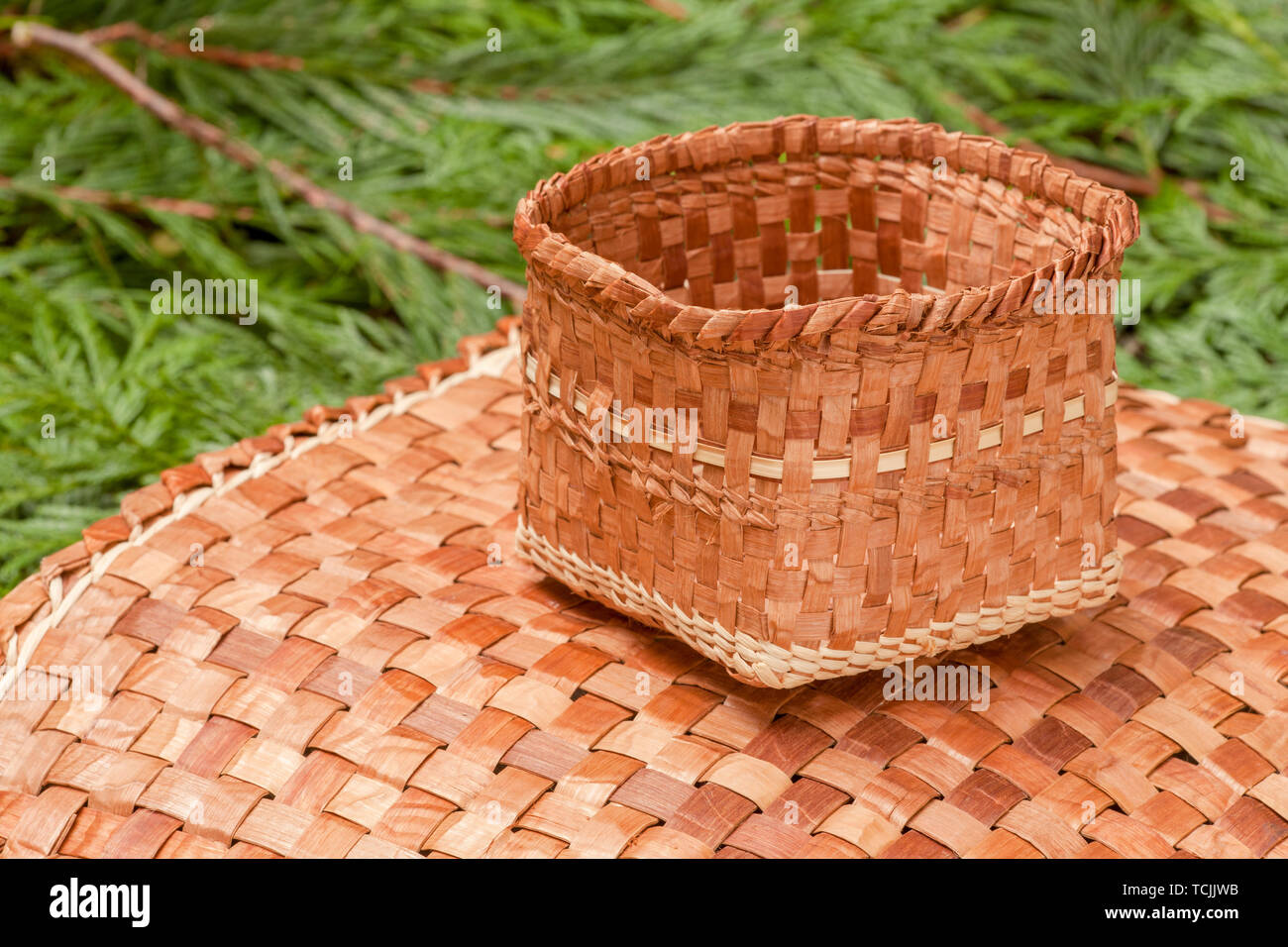 Hand-woven mat and basket made from the pliant inner bark of a Western Red Cedar tree, resting on Western Red Cedar branchlets. Stock Photo